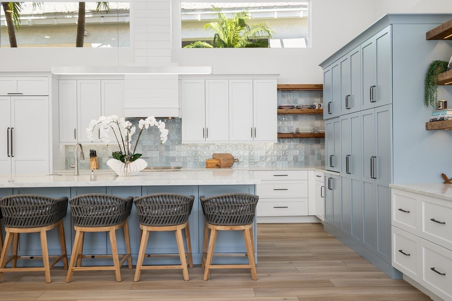 Blue kitchen island with woven bar stools and orchids