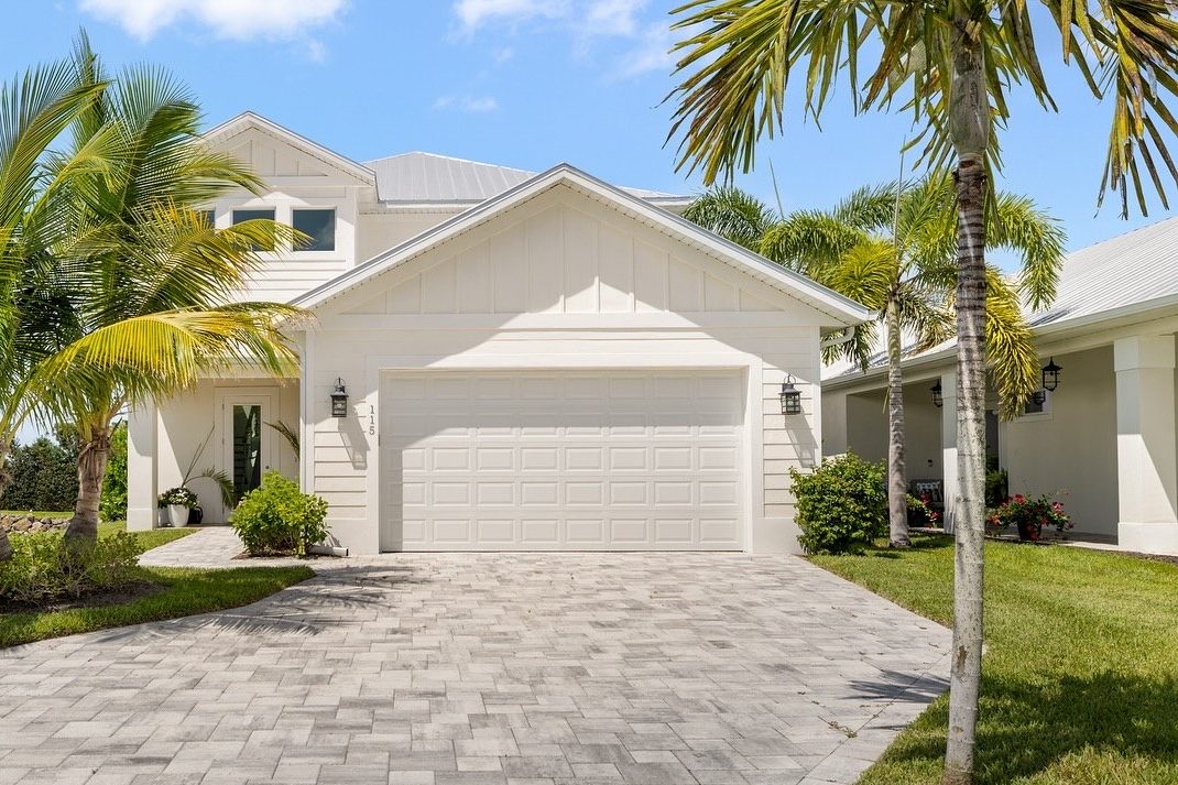 Front of a white coastal-style home with paver driveway and palms