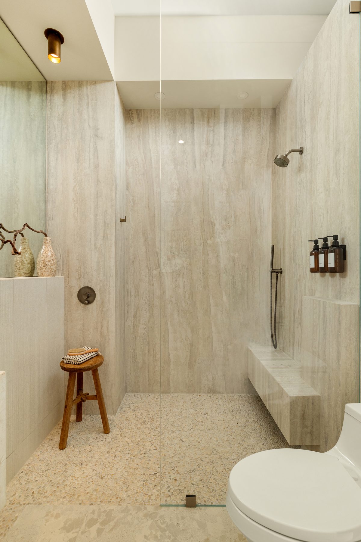 Travertine walk-in shower with a teak stool